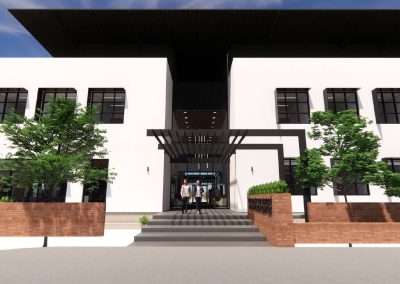 A modern, two-story building with large windows, a flat roof, and an entrance canopy. Two persons are walking towards the entrance, with trees flanking the pathway.